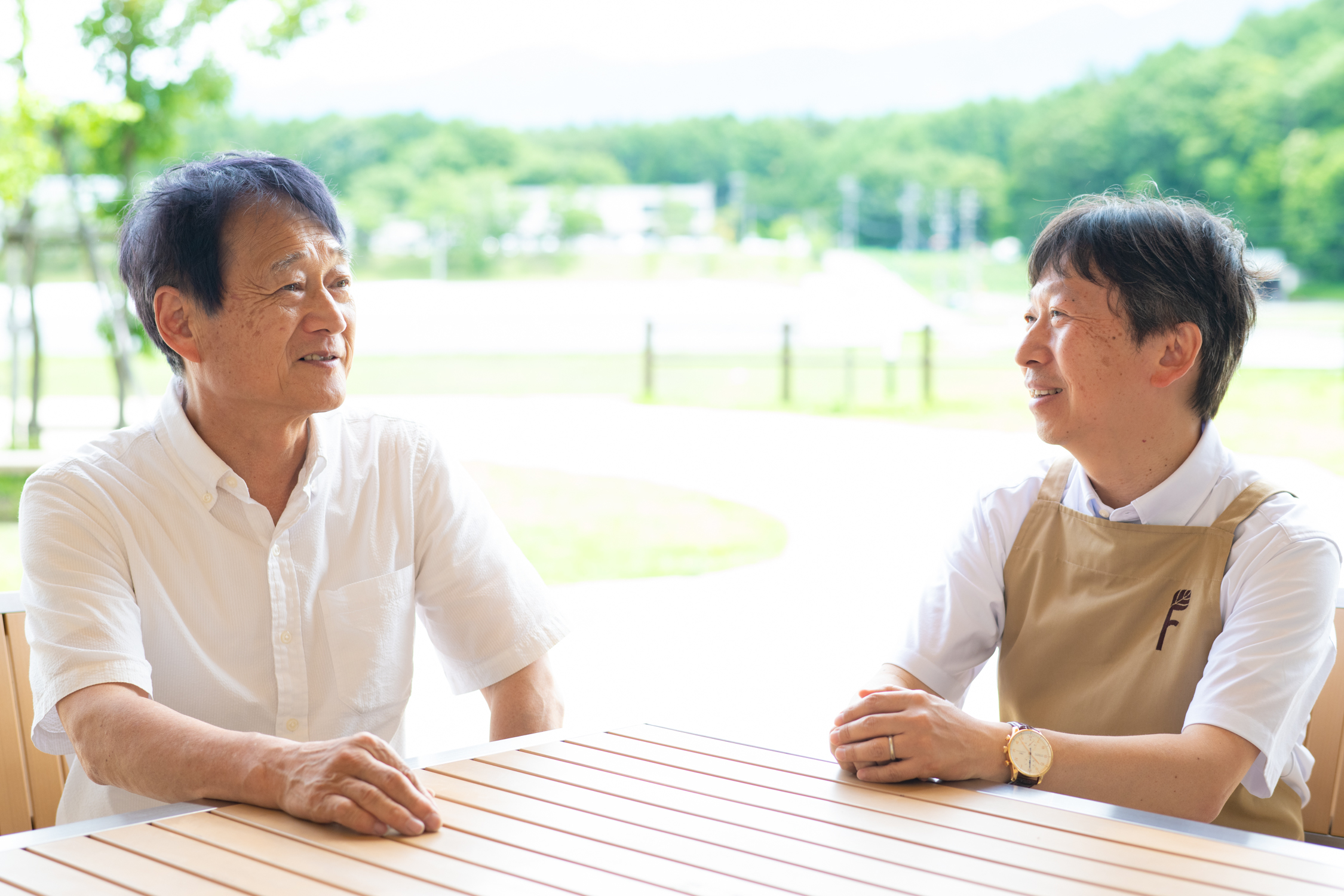 2人の男性がテーブルに座り、屋外で会話している。