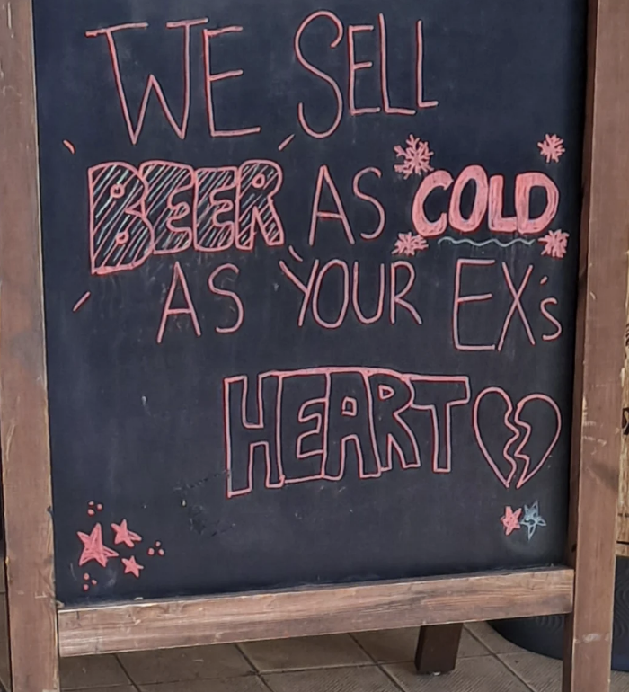 Sign reads: "We sell beer as cold as your ex's heart," with "beer," "cold," and "heart" emphasized in styled text. Heart image is split, symbolizing heartbreak