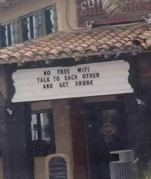 A sign on a building reads: "No free wifi. Talk to each other and get drunk."