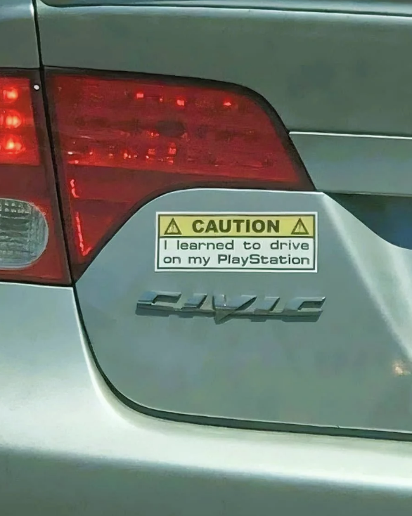 "Caution sign on car reads: 'Caution, I learned to drive on my PlayStation.' Honda Civic badge is visible."
