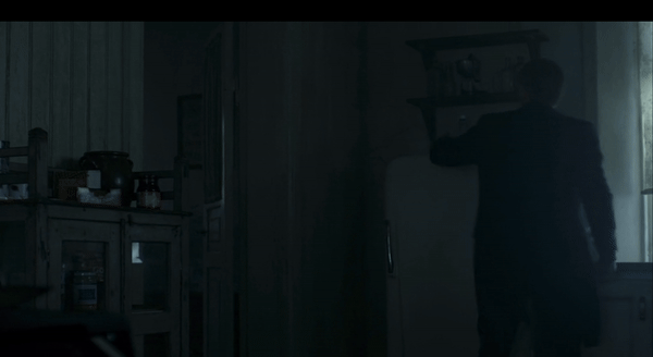 A person is standing in a dimly lit room, opening a cabinet, partially visible. Shelves with various items are seen in the background