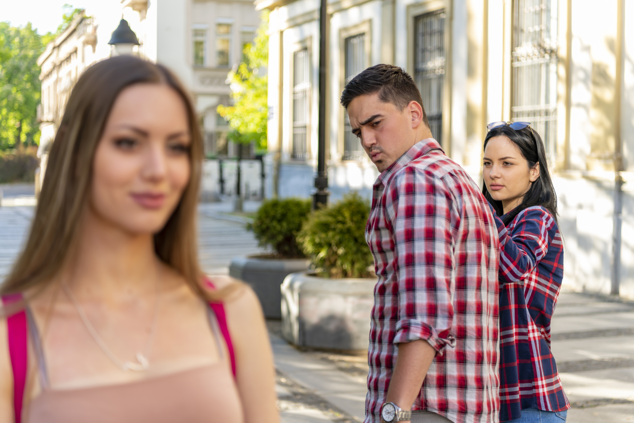Man checks out a woman passing by while holding hands with his upset partner