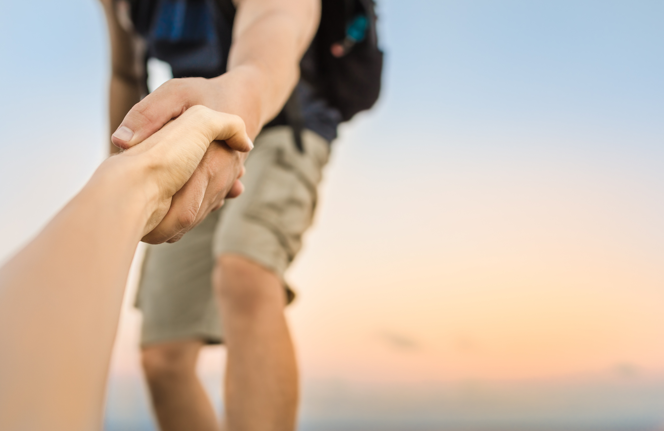 A person with a backpack reaches out to help someone up a hill, holding their hand