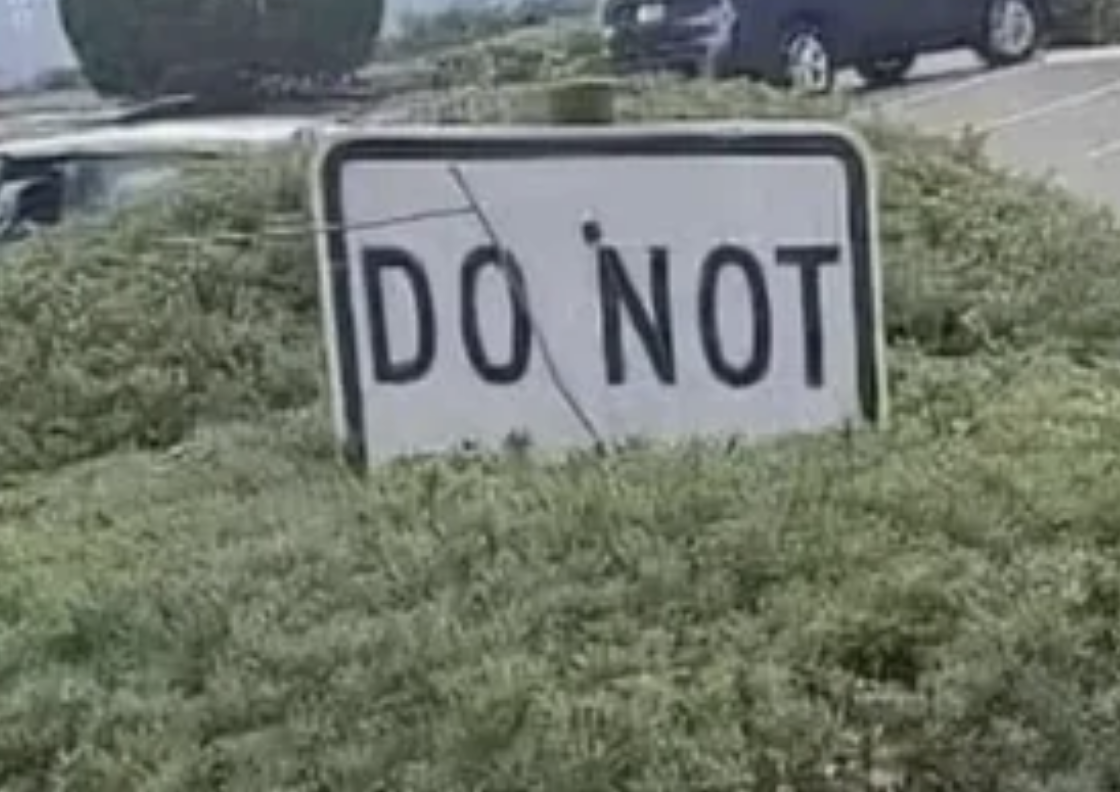 A rectangular sign among bushes reads "DO NOT."