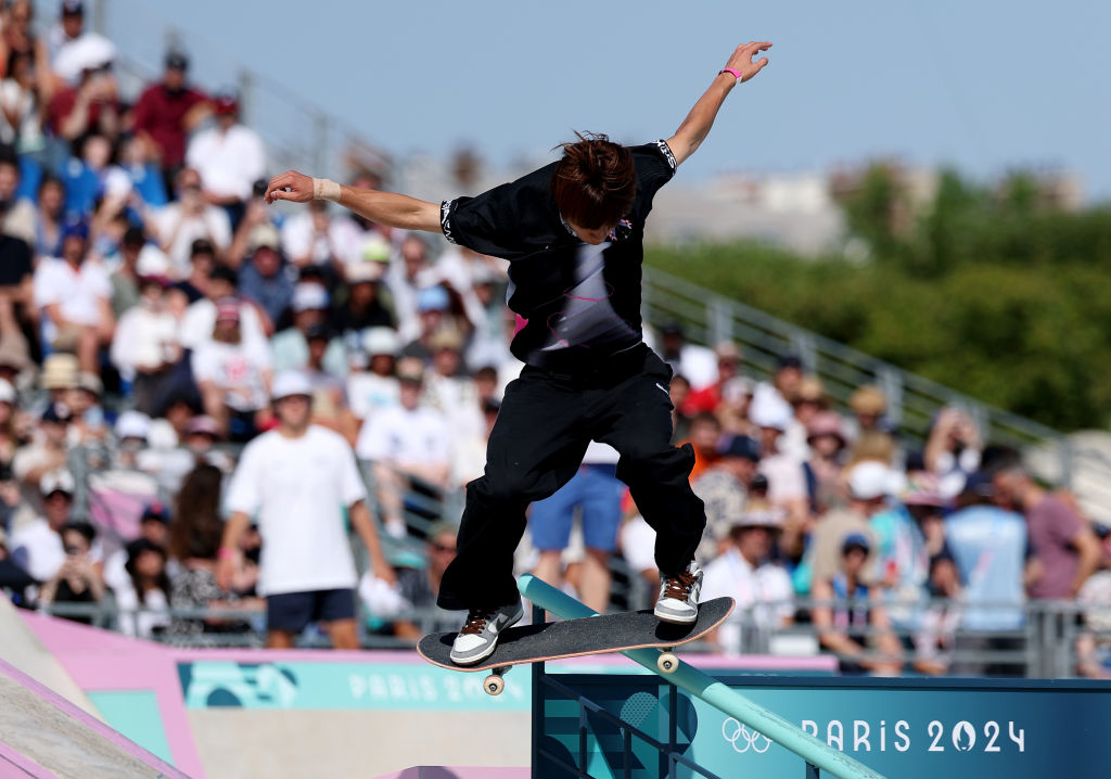 A skateboarder performs a trick on a rail at the Paris 2024 Olympic skateboarding event, with a crowd watching in the background