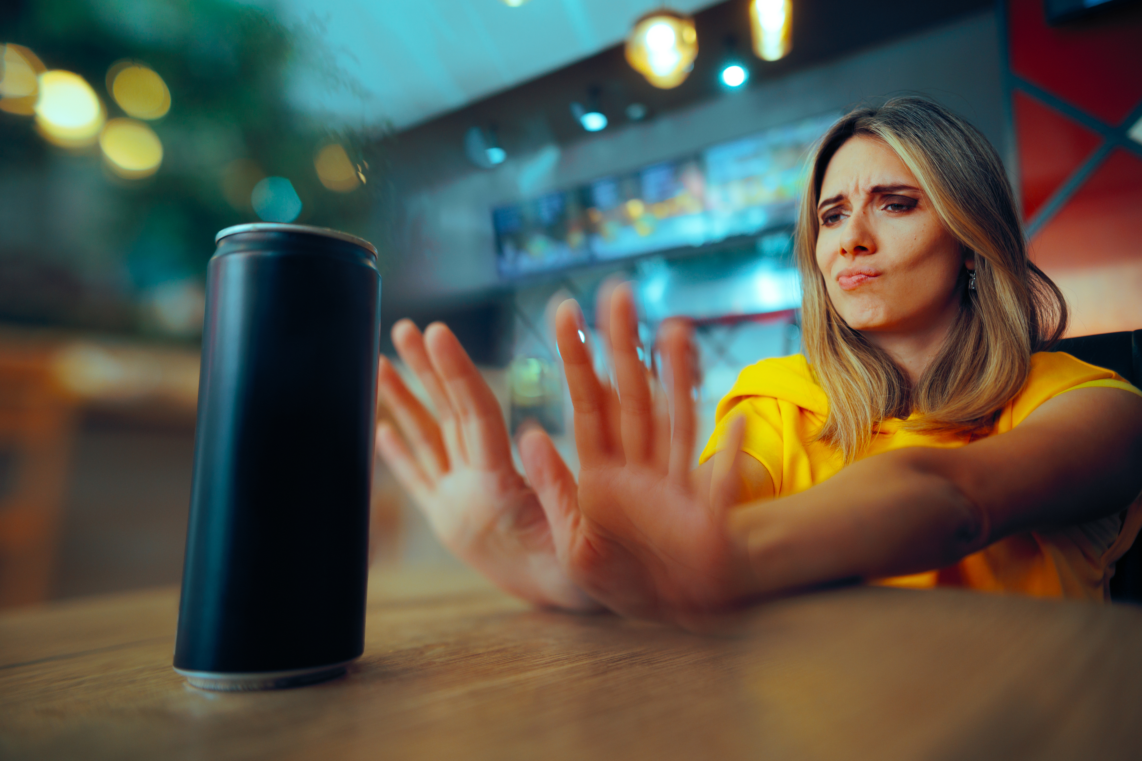 A woman in yellow shirt reaches out to a drink, appearing to express frustration or concern.