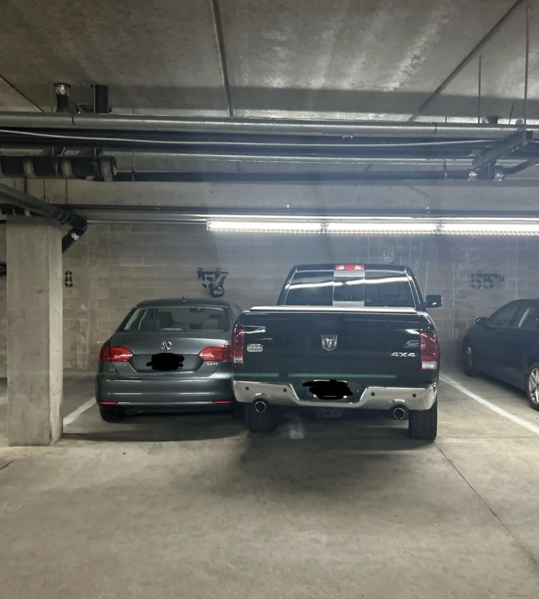 Two vehicles poorly parked in a tight underground parking space. One car is a sedan, and the other is a pickup truck, both partially obscured