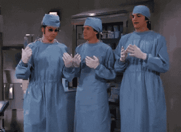 Danny Masterson, Topher Grace, and Ashton Kutcher dressed as doctors in blue scrubs and surgical hats, performing a comedic scene