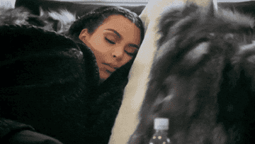 Kim Kardashian sleeping on a bed with fur pillows, water bottle visible