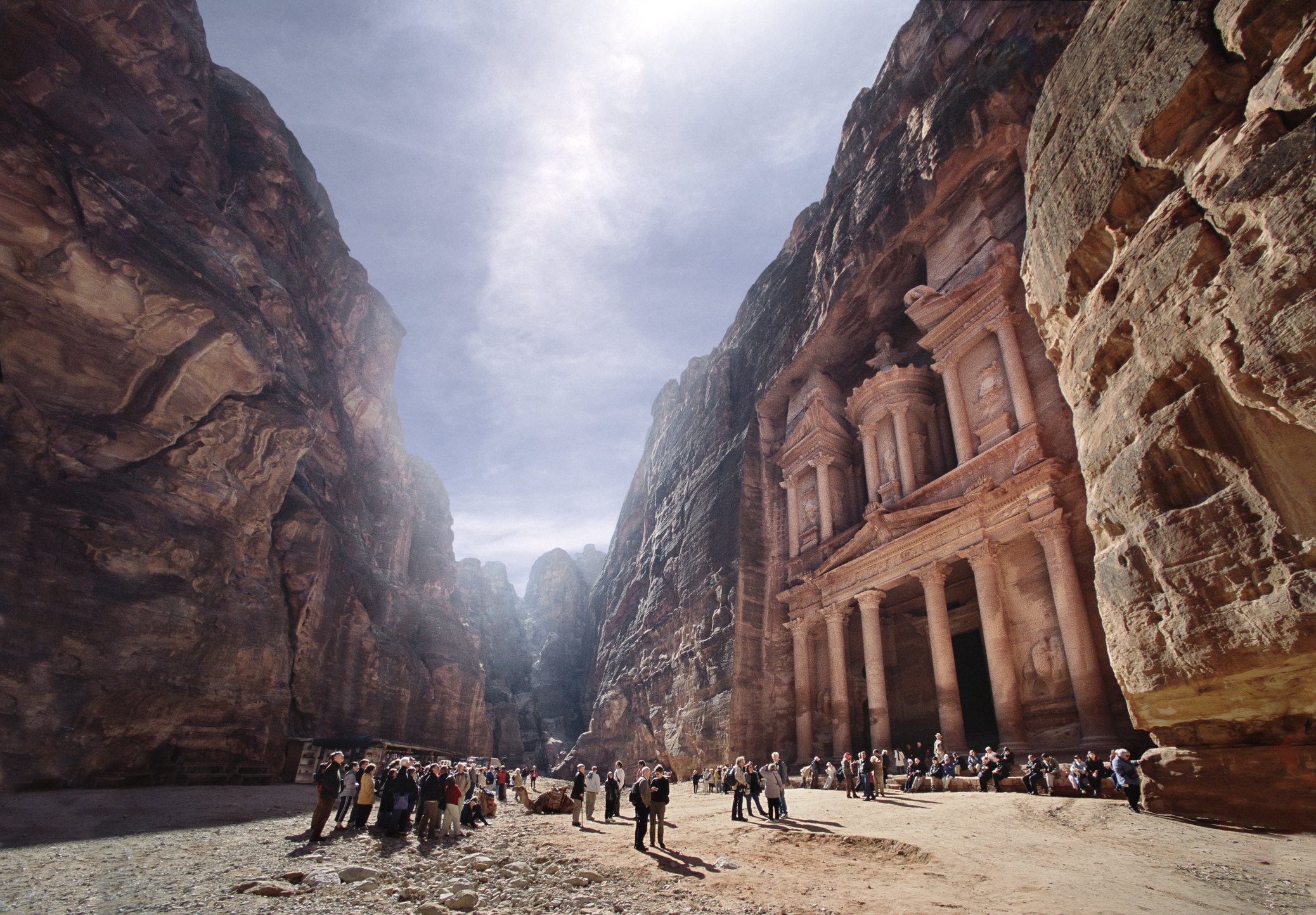 A crowd of people stands in front of the ancient stone-carved Al-Khazneh (The Treasury) in Petra, Jordan, nestled between towering rock formations