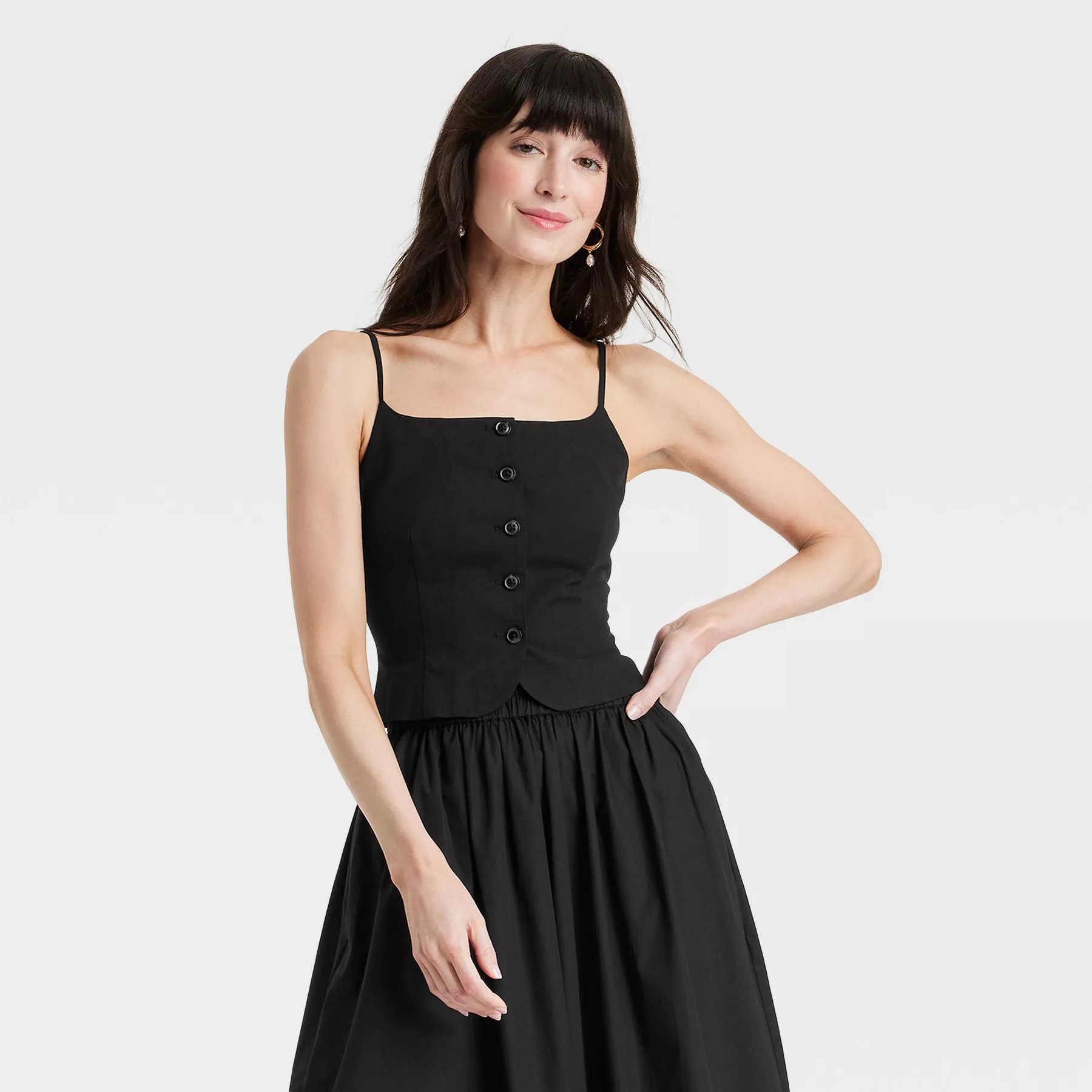 A model wearing a sleeveless, button-up black top and a matching black skirt