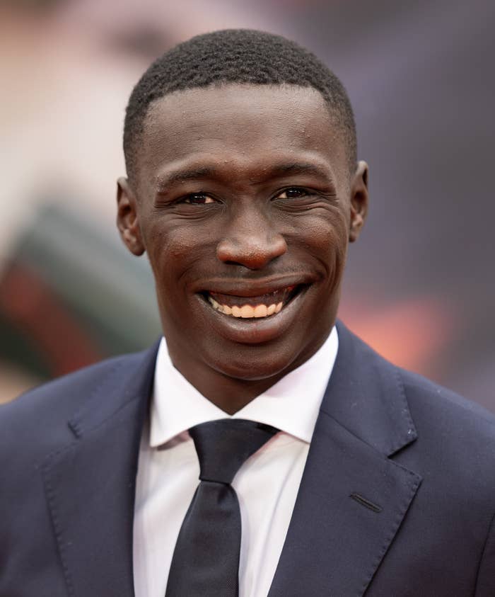 Khaby Lame smiles while wearing a dark suit and tie at a public event