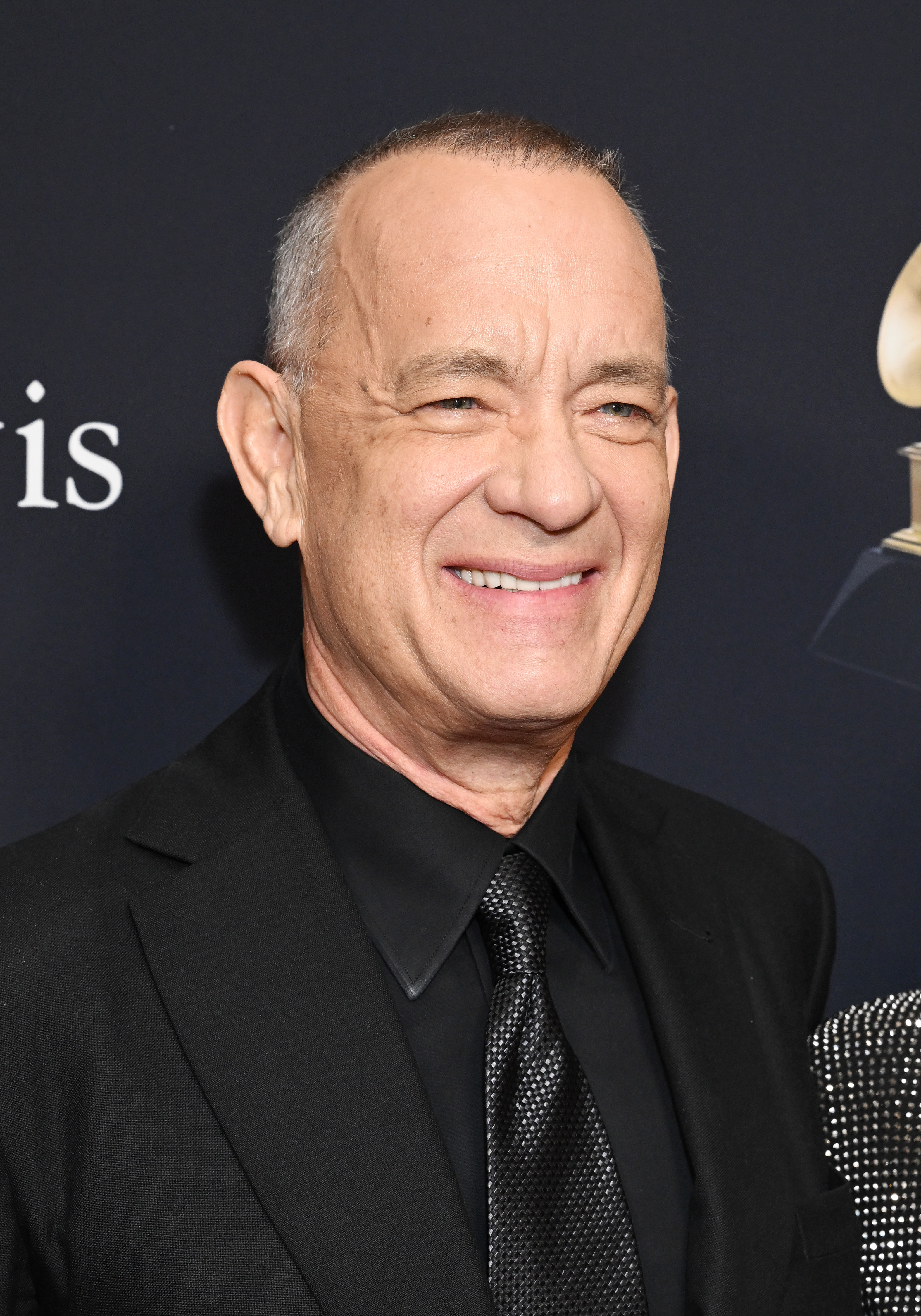 Tom Hanks smiling in a black suit and tie at a formal event