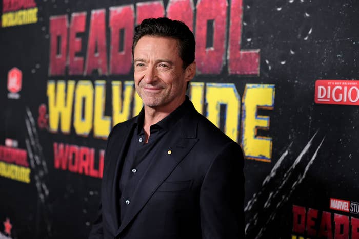Hugh Jackman smiles on the red carpet at the "Deadpool & Wolverine" world premiere, dressed in a stylish black suit