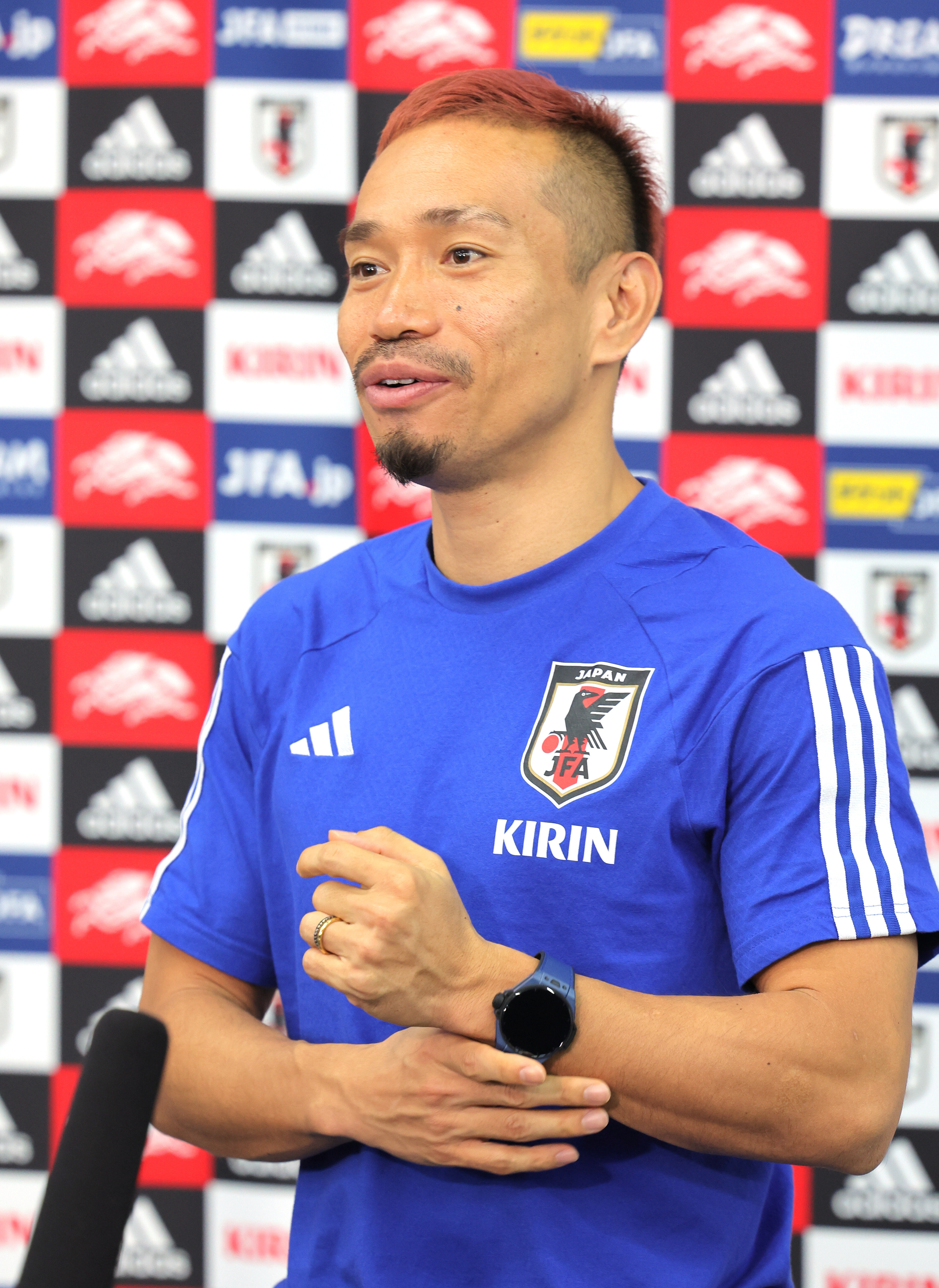 長友佑都が日本代表のサッカーユニフォームを着て記者会見に出席している。背景にはスポンサーのロゴが並んでいる。