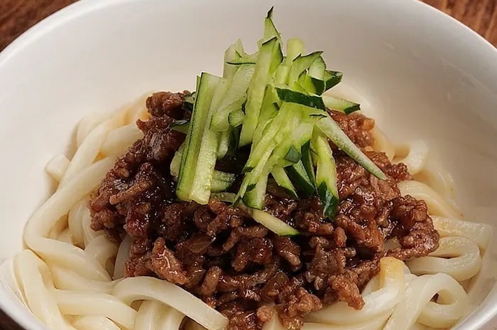 白いボウルに盛られたうどんの上に、ひき肉とキュウリがトッピングされています。