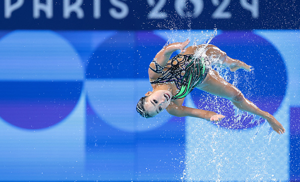 An artistic swimmer performs an acrobatic routine in mid-air at the Paris 2024 event