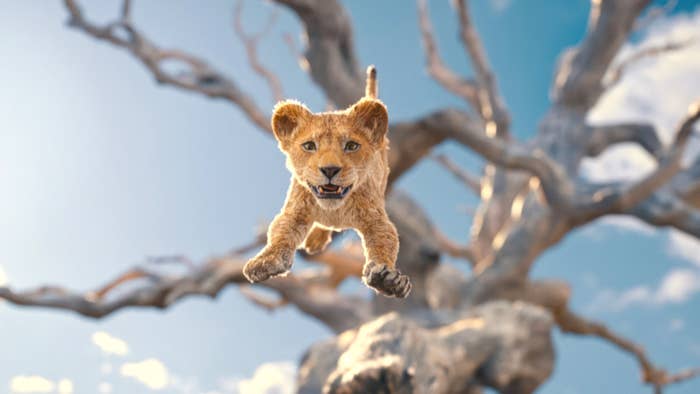 Animated baby lion cub Simba from The Lion King jumps in the air against a background of a large, leafless tree and blue sky