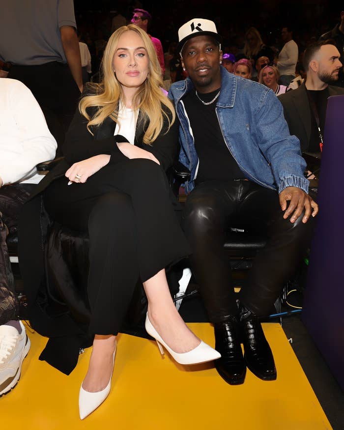 Adele and Rich Paul are seated together at an event. Adele is wearing a black outfit with white heels, while Rich Paul is dressed in a denim jacket and black pants