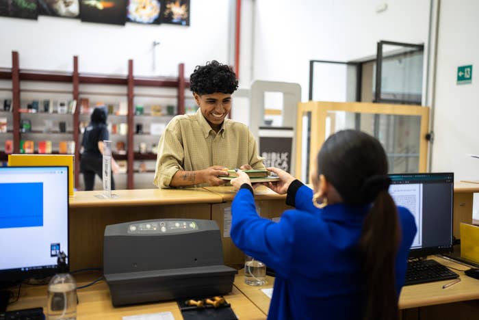 Person receiving documents from a cashier at a public service counter, with a background of bookshelves and administrative items
