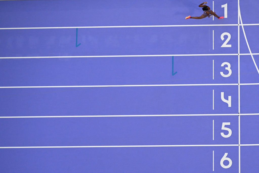 Overhead shot of a track athlete in mid-jump above the starting lines at a track, appearing to leap over the number 1 lane