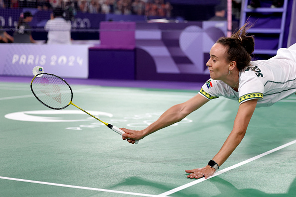 A badminton player dives and reaches out with her racket to hit the shuttlecock during a game at the Paris 2024 event