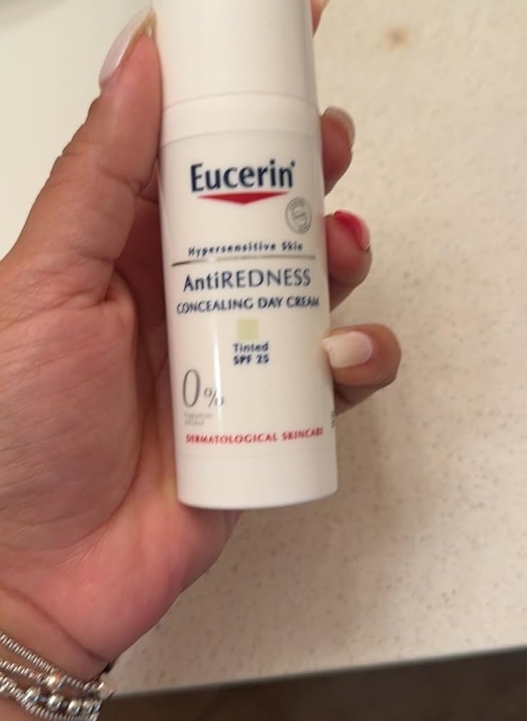 Hand holding a bottle of Eucerin Anti-Redness Concealing Day Cream, Tinted SPF 25 for Hypersensitive Skin on a bathroom counter