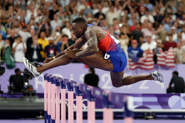 Male athlete in action during a hurdle race at a track event, with a crowd in the background