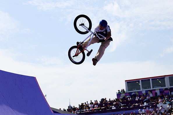 Person performing an aerial trick on a BMX bike on a ramp with a crowd watching in the background