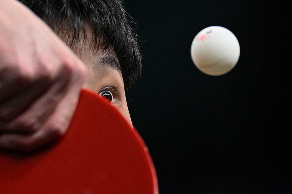 A close-up image of a ping pong player hitting a ball with intense focus. The player's paddle and eye are clearly visible, showcasing their concentration