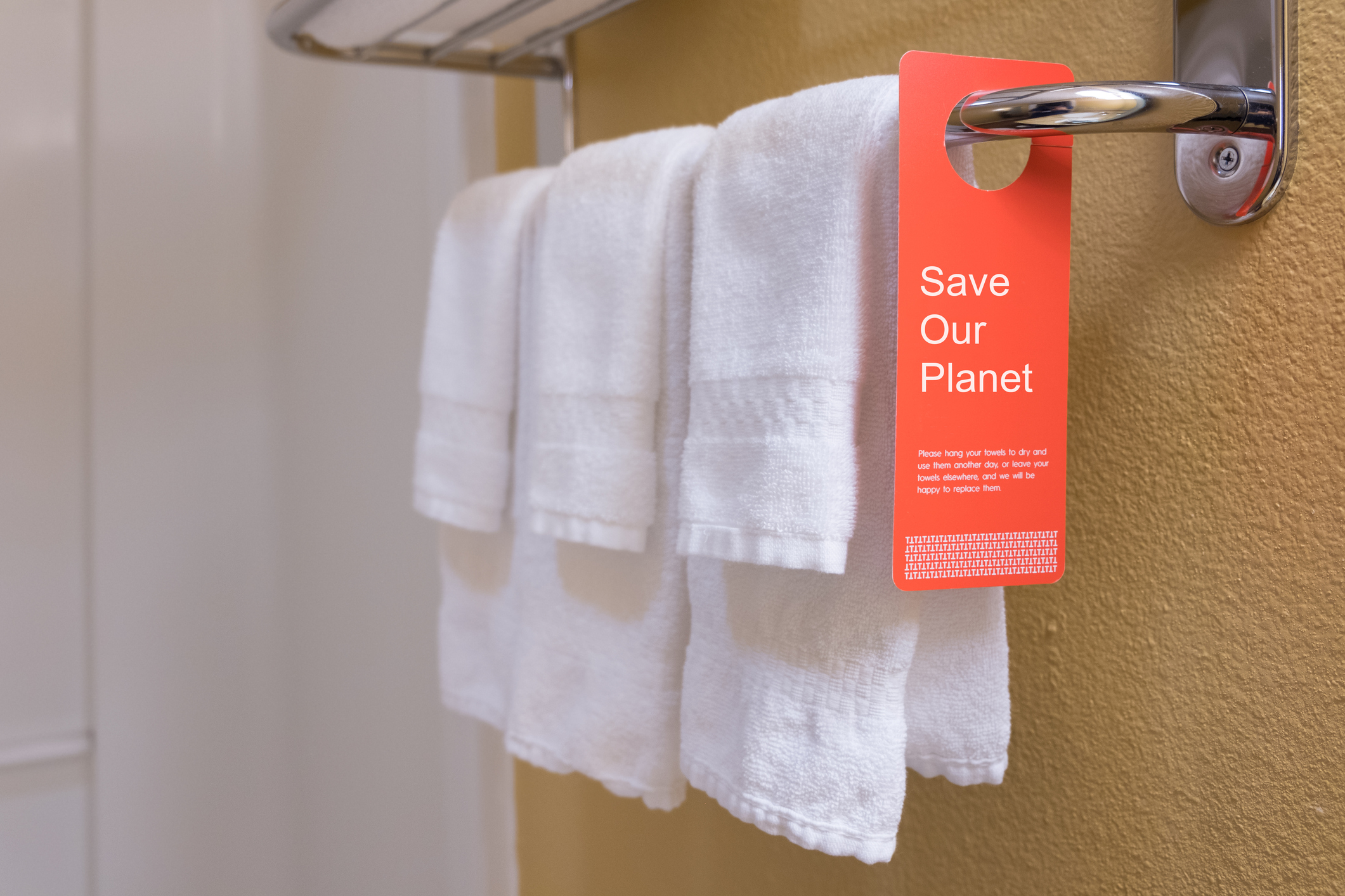 Towels hanging on a rack with a red tag that reads &quot;Save Our Planet&quot; urging reuse to save water and energy