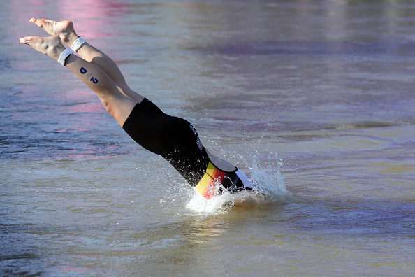 Person in a black and multi-colored wetsuit making a dive into the water during a sports event, identified by a number 3 on their lower leg