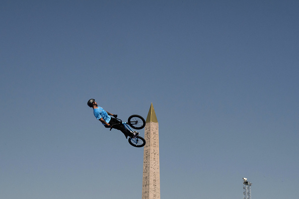 Person performs a mid-air stunt on a BMX bike in front of an obelisk monument against a clear sky