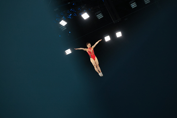 A gymnast in mid-air performs a routine under bright stage lights