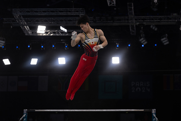 Gymnast performs a skill on horizontal bar during a competition. The background displays "Paris 2024."