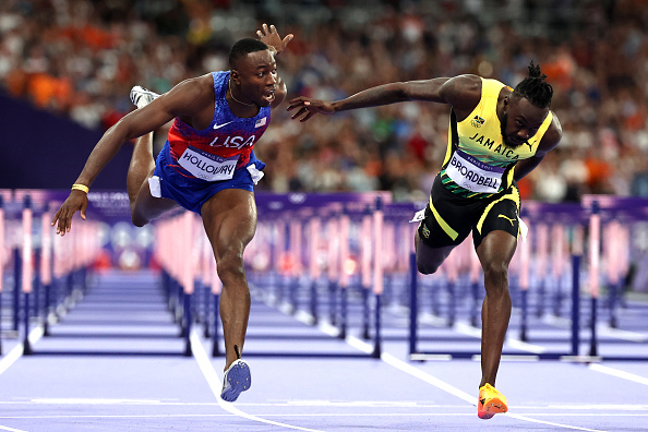 Team USA's Freddie Crittenden III and Jamaica's Damion Thomas mid-race during a hurdles event at a track and field competition. Both athletes are in action