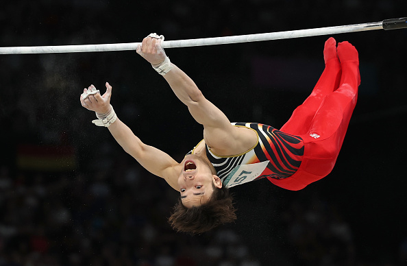 Gymnast Daiki Hashimoto performs a thrilling high bar routine in mid-air, wearing a sleeveless top and red pants