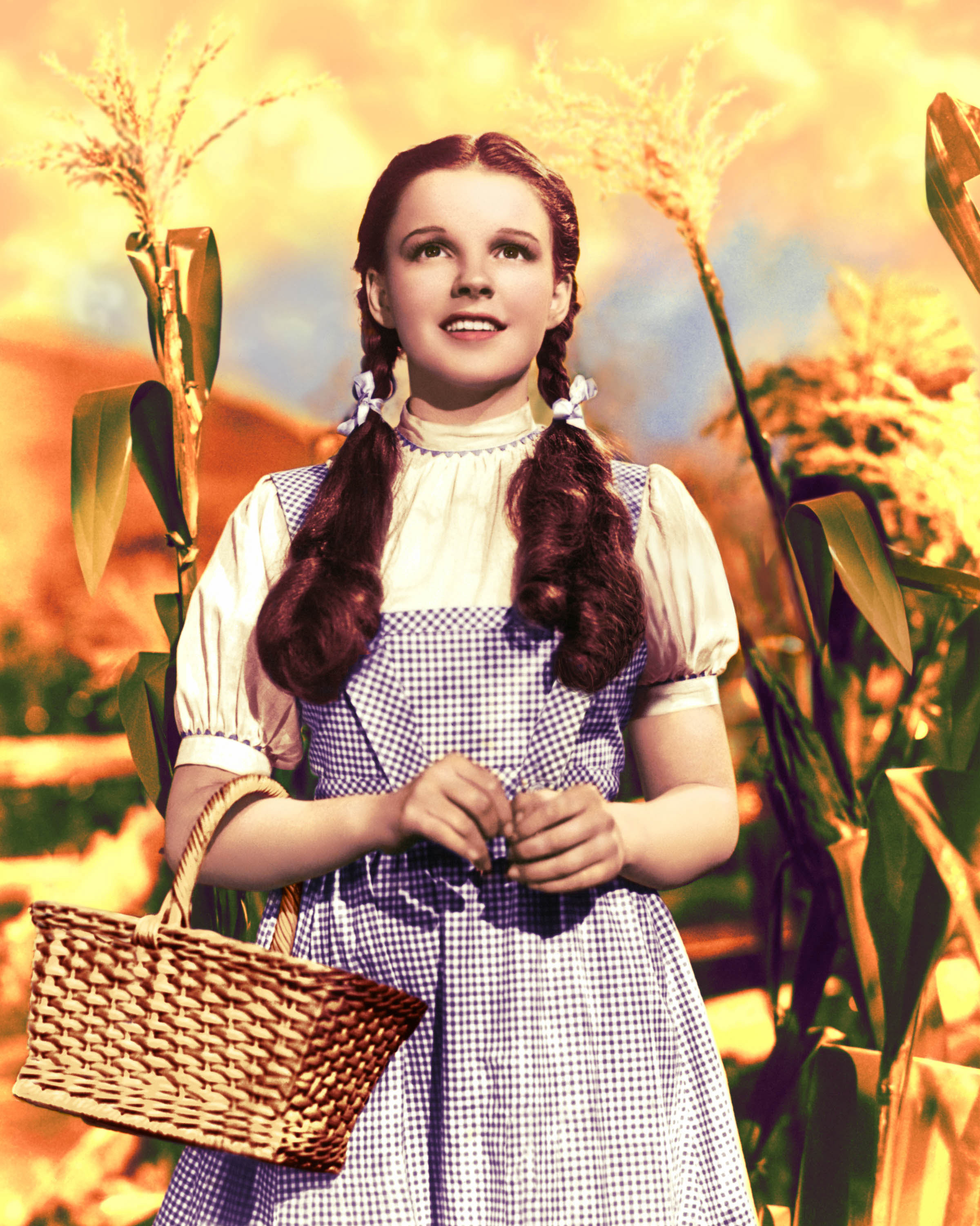 Judy Garland as Dorothy from The Wizard of Oz, wearing a gingham dress and holding a basket, stands in a cornfield looking upward
