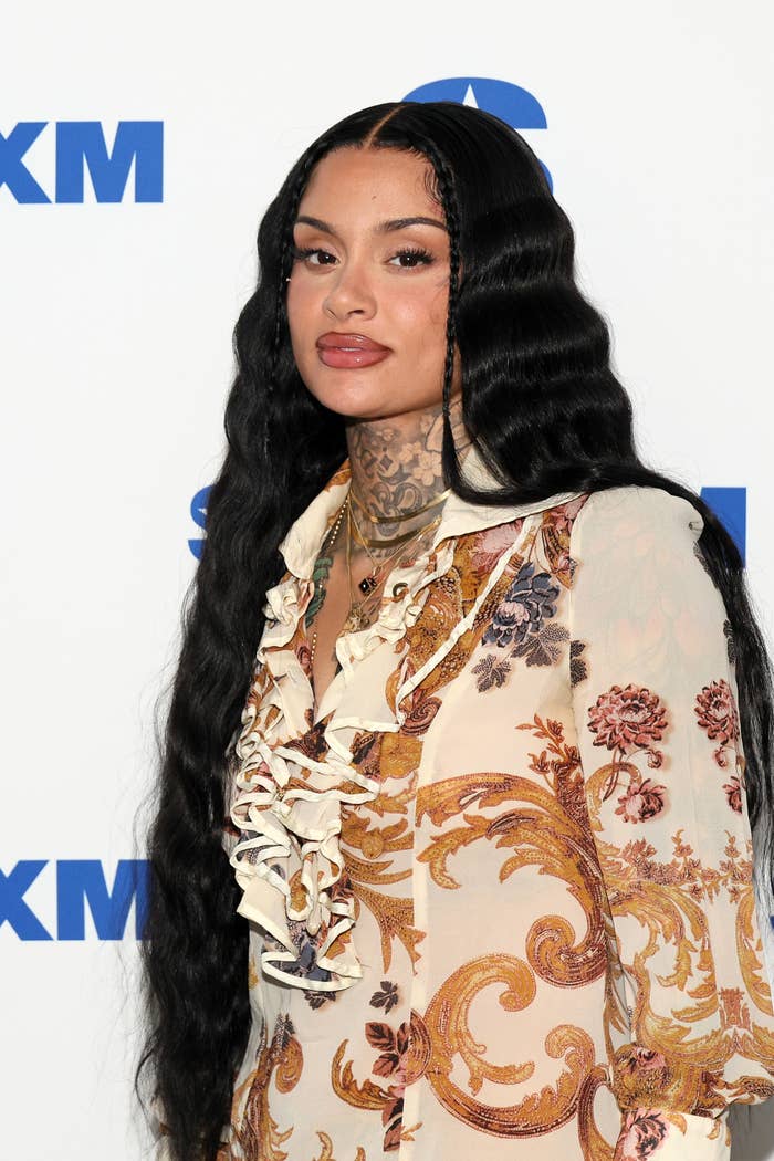 Kehlani poses gracefully with wavy long hair, wearing a stylish ruffled dress with intricate patterns, at a SiriusXM event