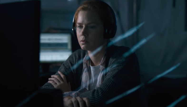 Amy Adams is focused, wearing headphones and a sweater, and sitting in front of a computer screen