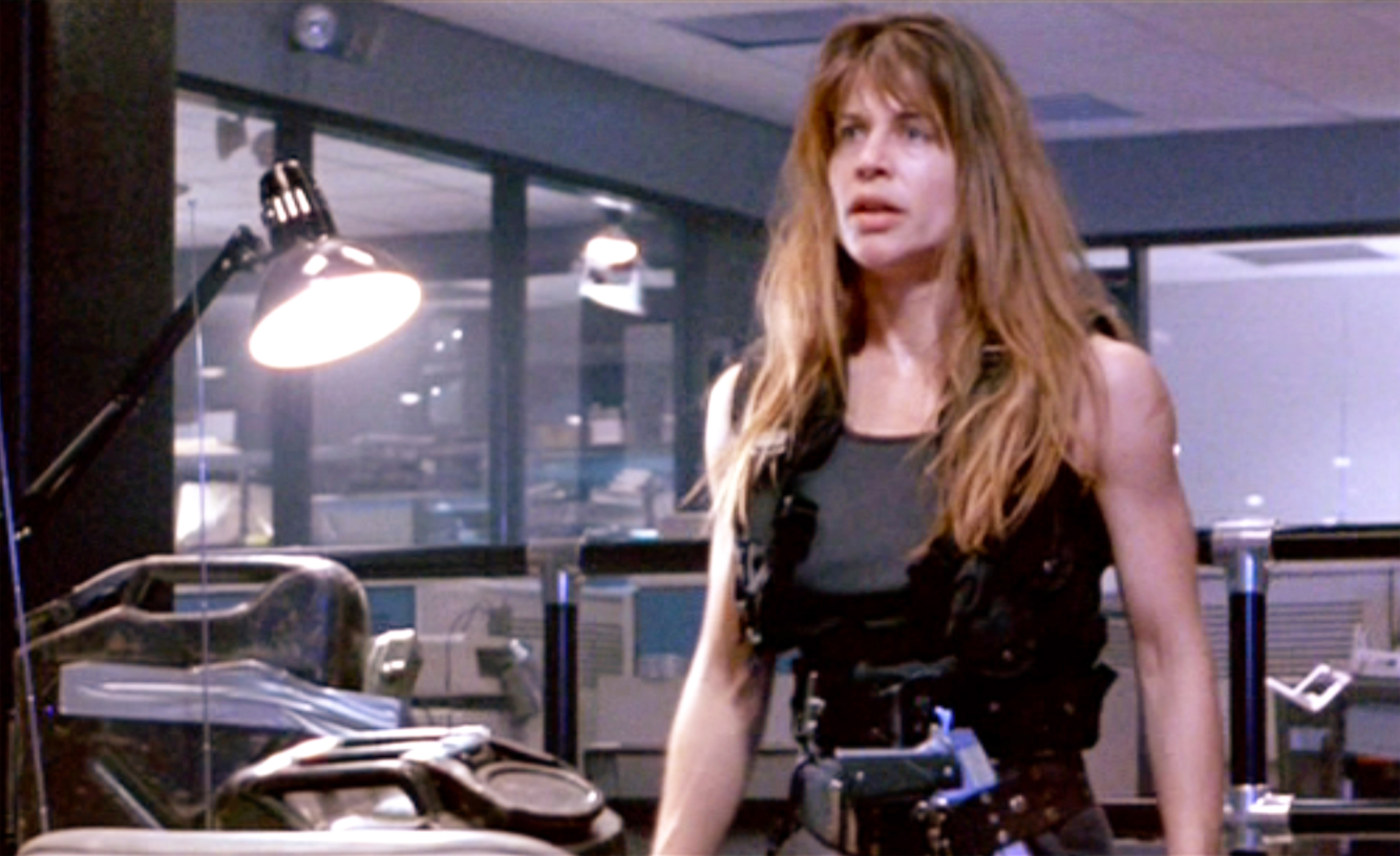 Linda Hamilton as Sarah Connor in a tactical vest with a determined expression in an office setting from the movie Terminator