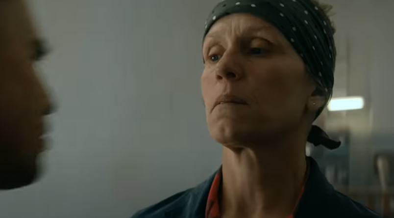 Frances McDormand, with a serious expression, wearing a bandana and casual work attire