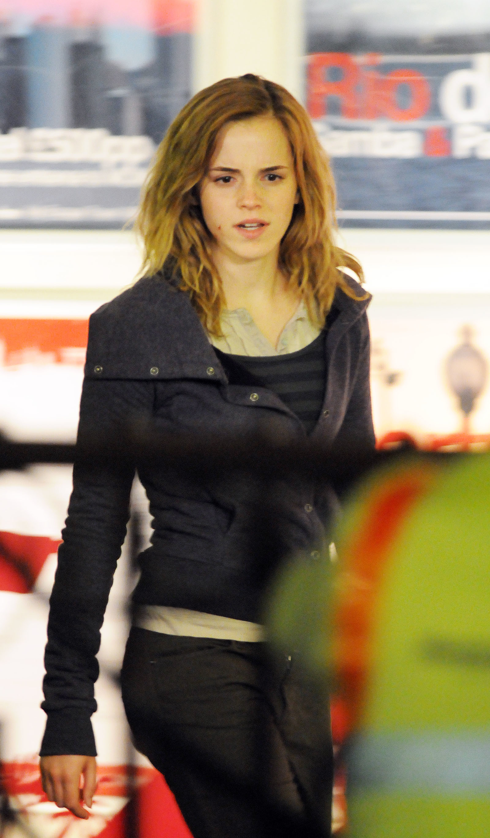 Emma Watson is casually dressed, walking indoors near posters on the wall