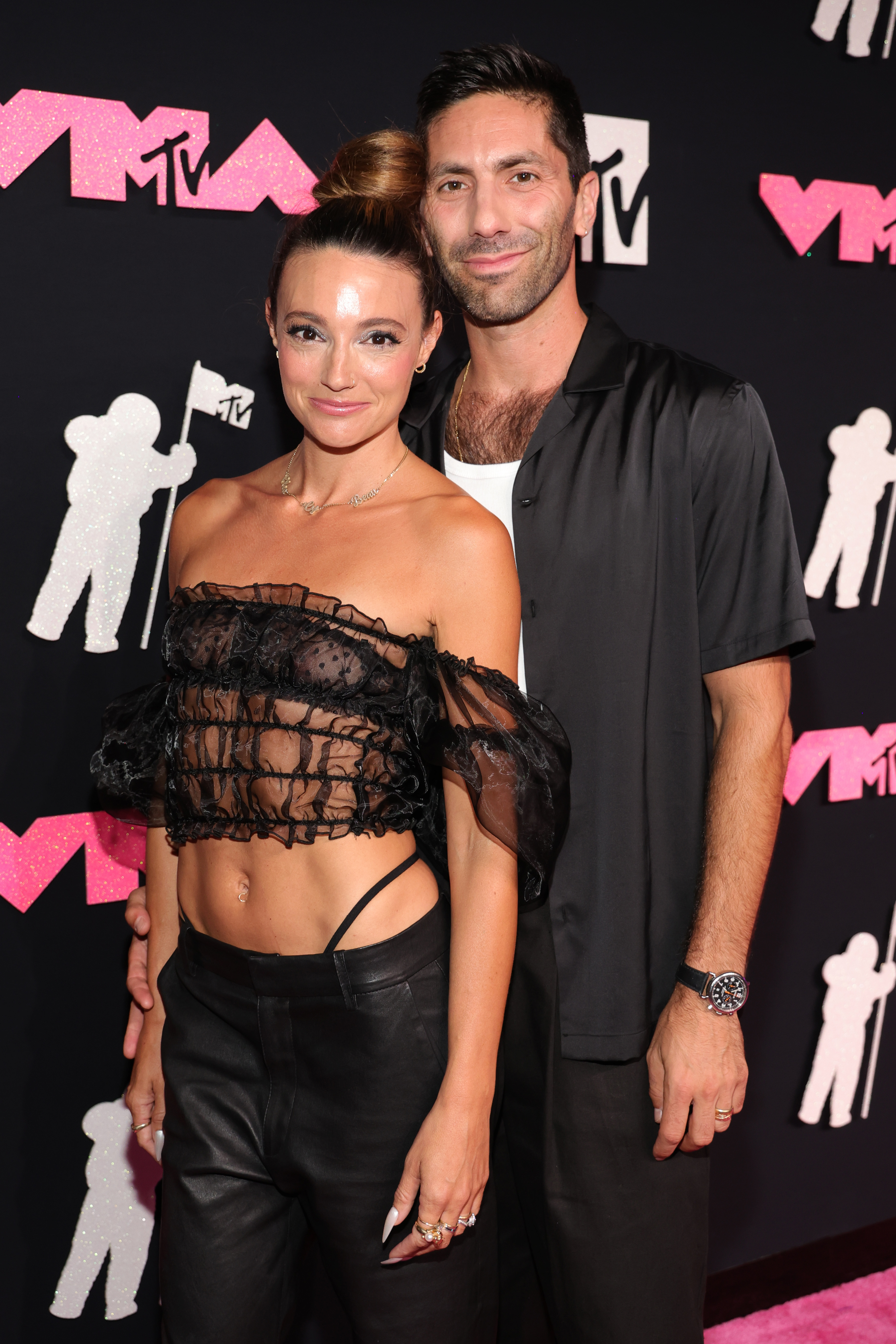 Jenna Johnson and Val Chmerkovskiy at the MTV event. Jenna wears an off-shoulder, sheer top with black pants. Val wears a black shirt over a white top and black pants