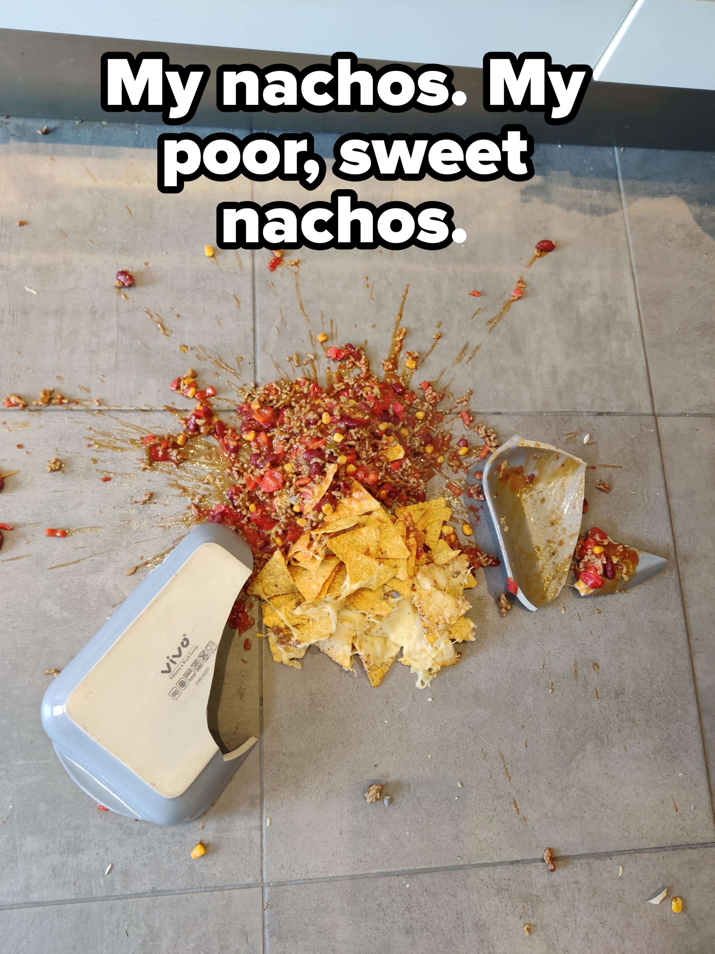 Spilled nachos with salsa and corn on a tiled floor; a broken Vivo container is next to the mess