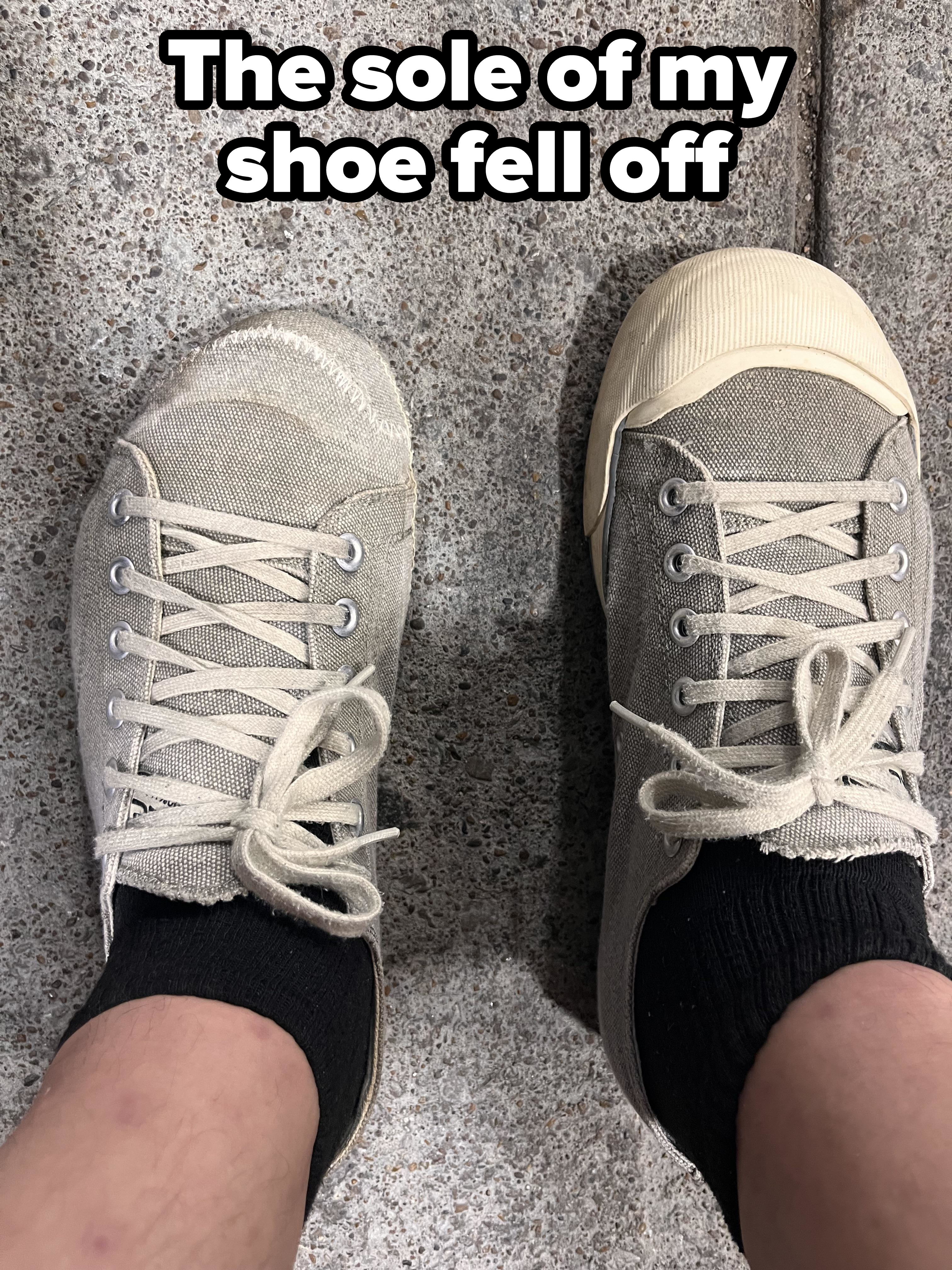 Two feet with black socks wearing mismatched, worn sneakers on a speckled concrete surface