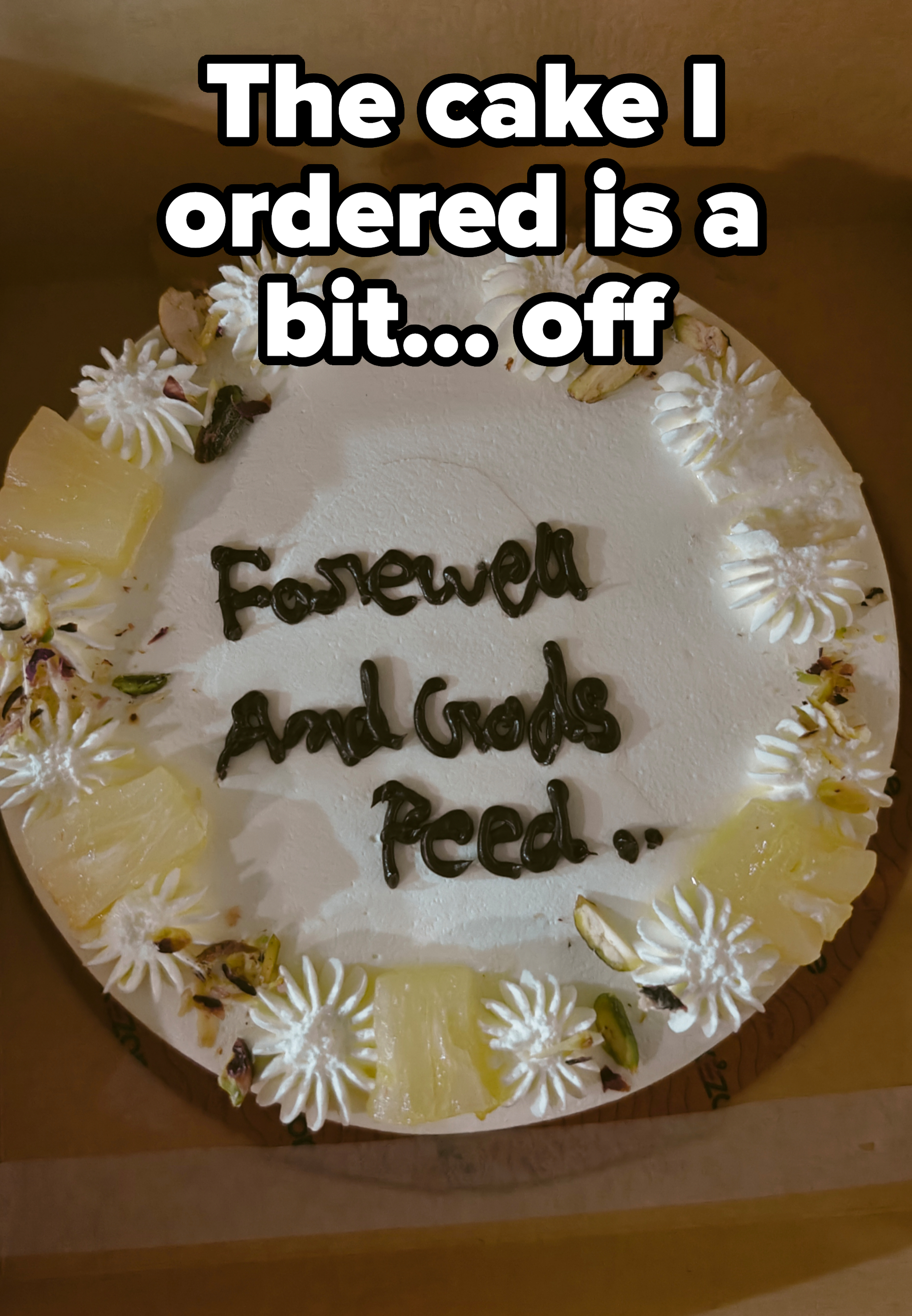 Round cake with white frosting, decorated with cream swirls, pistachios, and pineapple slices. Text on cake reads "Farewell And Gods Peed.."