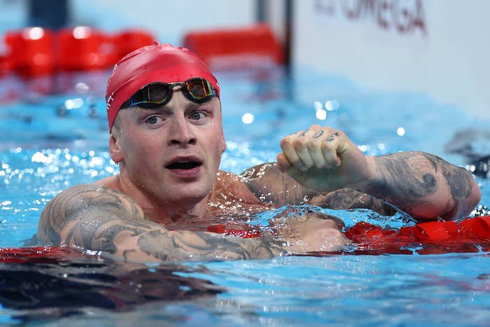 Adam Peaty is in a swimming pool, wearing goggles and a swim cap, raising his fist in celebration