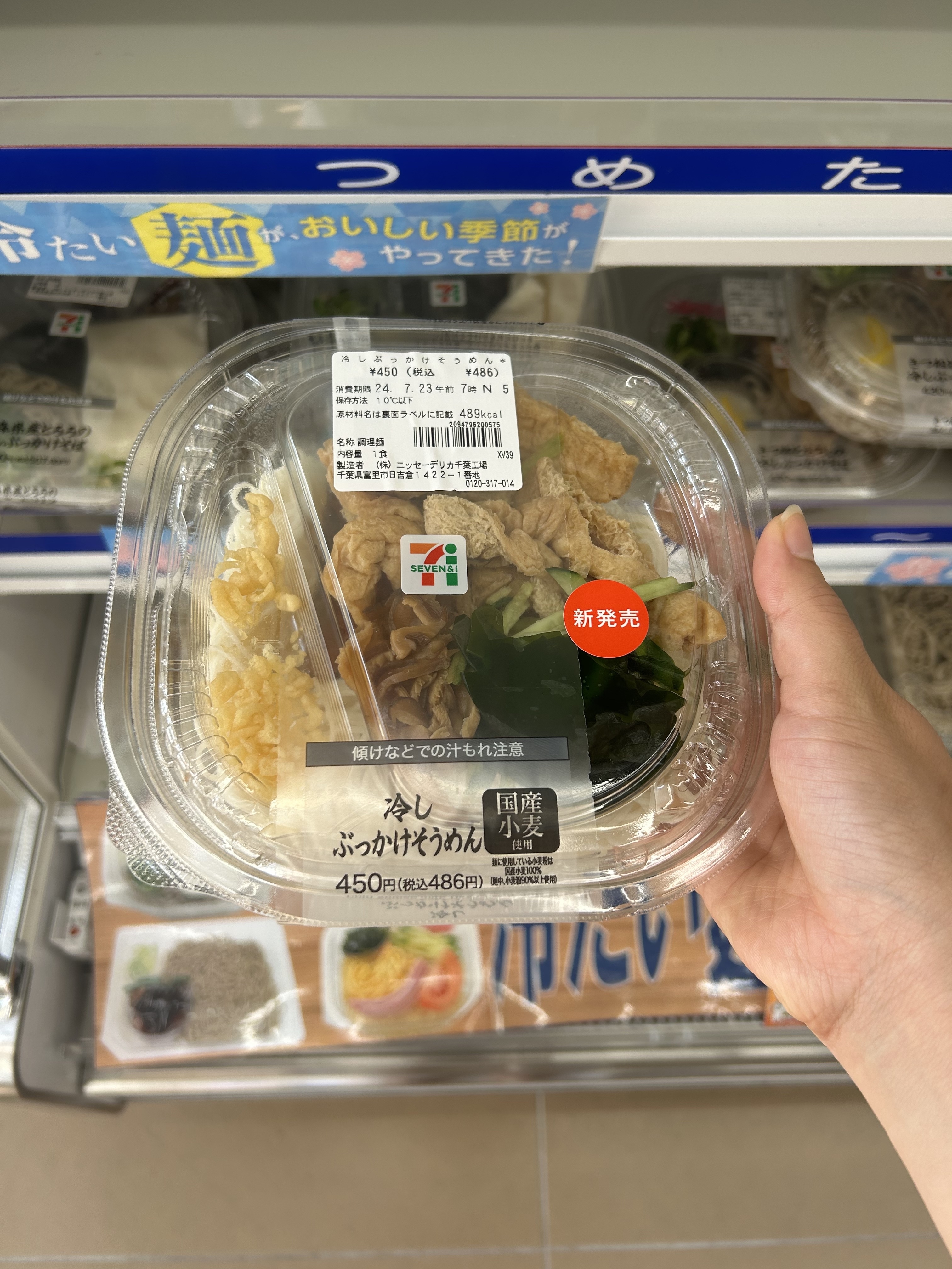 Person holding a packaged salad bowl from 7-Eleven with rice, vegetables, and a clear lid in a convenience store