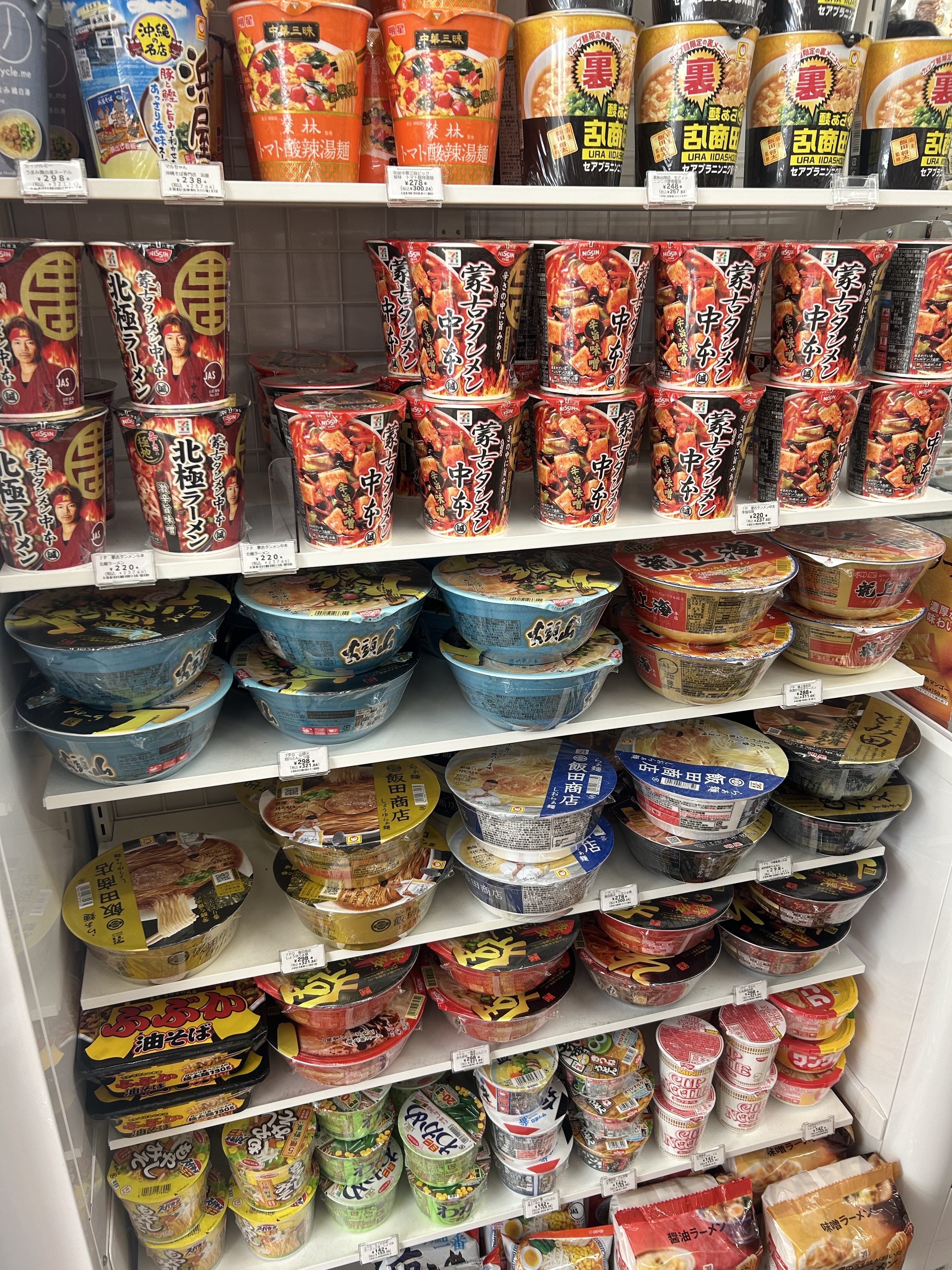 A store shelf filled with various brands and types of instant noodles, arranged in multiple rows and columns